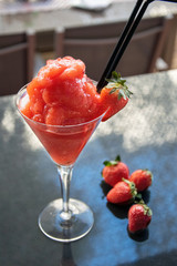 a tasty frozen strawberry daiquiri cocktail alongside some fresh strawberries 