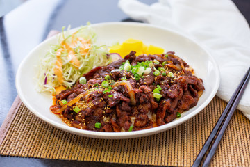 A view of a plate of Korean style spicy grilled pork over rice, in a restaurant or kitchen setting.