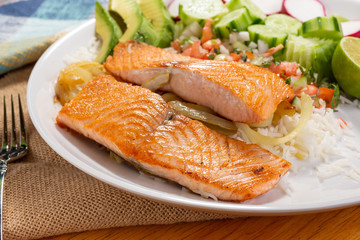 A closeup view of salmon fillets on a dinner plate, in a restaurant or kitchen setting.