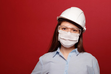 coronavirus pandemic, close-up portrait of young woman on red background in protective medical mask, builder architect  in protective medical mask