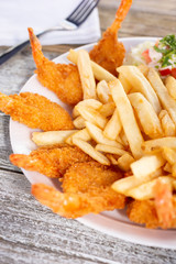 A plate of deep fried shrimp surrounding french fries, in a restaurant or kitchen setting.