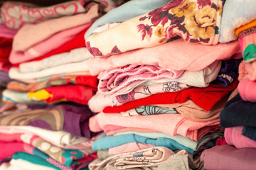Lots of folded colorful childrens clothes aligned in rows in a drawer, closet. Many simple kids clothing with patterns stacked neatly in a wardrobe closeup shot, abstract background texture, nobody