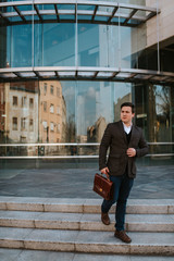 Young handsome caucasian businessman in front of company with bag in hand