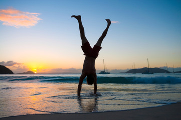 Scenic sunset silhouette of unrecognizable young man doing a cartwheel on the shore of a tropical beach