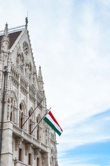 Fototapeta na wymiar Building of the Hungarian Parliament Orszaghaz in Budapest, Hungary. The seat of the National Assembly. House built in neo-gothic style. Waving flag of Hungary on the house. Hungarian concept
