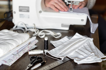 Woman sews protective antivirus masks at home on a sewing machine
