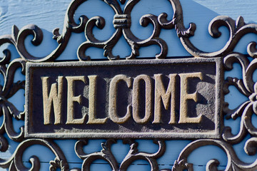 dekoratives gusseisernes schild mit schriftzug welcome und ornamenten auf grauer wand gold braun im sonnenlicht schatten