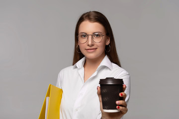 young businesswoman in white shirt with yellow folder and coffee to go isolated on grey background  