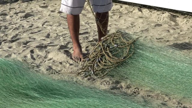 South American fisherman wrapping the net fishing on his feet, detail of feet and net, sand background