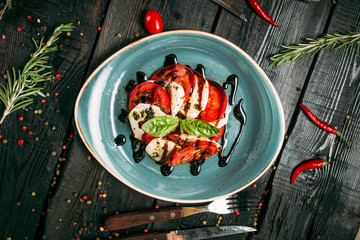 Top view on fresh appetizing caprese salad with tomatoes and mozzarella on a blue plate on the wooden background, horizontal