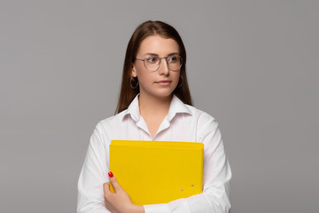 Obraz premium smiling young businesswoman in white shirt with yellow folder isolated on grey 