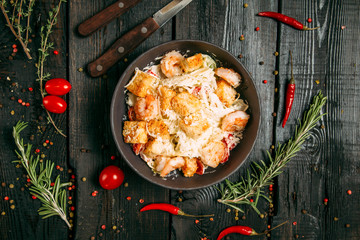 Top view on fresh caesar salad of vegetables, chicken and cheese in a dark bowl on the dark wooden background, horizontal