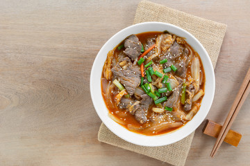 top view of stir fried beef with kimchi in a ceramic bowl on wooden table. asian homemade style food concept.