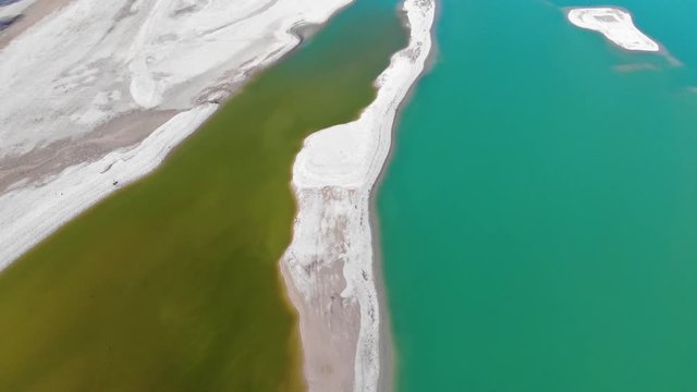 Uferbereich des noch nicht vollständig gefüllten Forggensees mit verschiedenen Wasserfärbungen von grünlich bis türkies in der Draufsicht im Vorwärtsflug