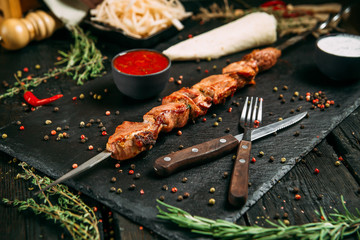 appetizing duck kebab stick with red sauce and pickled onion on a black board on a dark wooden background, side view, horizontal