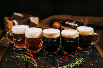 Dark and ginger beer set in mugs on the wooden background with herbs and pepper, horizontal, side...