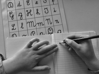 hands of a kid, doing homework, learning to write cursive alphabet with a board