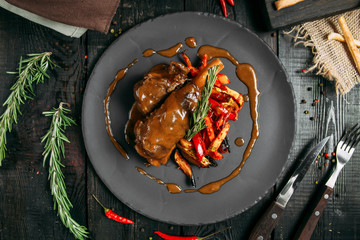 Top view of appetizing stewed veal in a sauce with vegetables on a black plate on a dark wooden background, horizontalbackground, horizontal