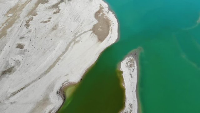 Uferbereich des noch nicht vollständig gefüllten Forggensees mit verschiedenen Wasserfärbungen von grünlich bis türkies in der Draufsicht im Rückwärtsflug