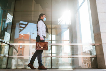 
Young businessman walking with gloves and face mask in front of company. COVID - 19 virus protection