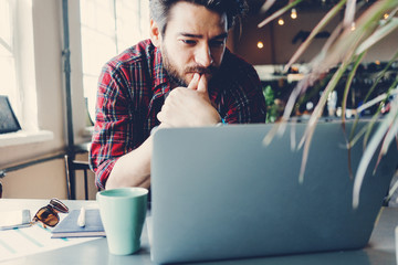 Man working with laptop. Entrepreneur wearing casual clothes and stubble in big spacious bright room. Workspace on the table