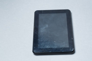 Black scratched tablet with a protective film on a gray background. Protect your device screen