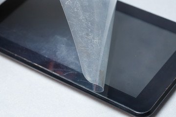 Black scratched tablet with a protective film on a gray background. Protect your device screen