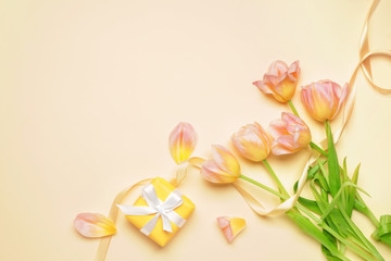 Gift and beautiful flowers on color background