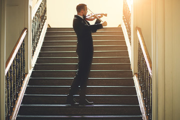 young caucasian male violinist practice music performance on the stairs in the hall, handsome guy...