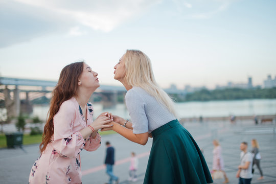 Two cute girls sending air kisses to eacn othes. Outdoor photo of young women.