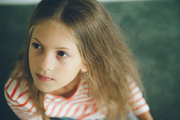 pensive beautiful little caucasian girl with long hair sitting at home thinking idea mental creative concept