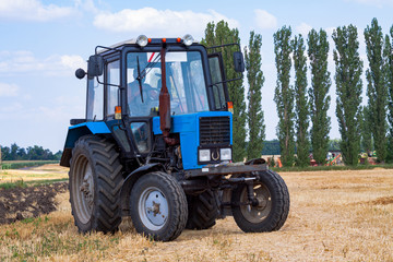 tractor makes big straw roll on yellow field at summer day
