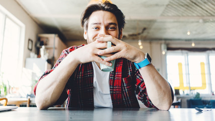 Portrait of handsome young smiling man with cup. Sitting in art design bright interior
