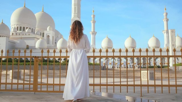 Silhouette back view. happy young woman tourist look at white Sheikh Zayed Grand Mosque Center. Girl in long dress enjoys arab architecture. Background Modern buildings Abu Dhabi United Arab Emirates