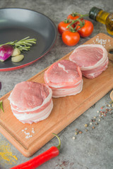 Three raw filet Mignon on a wooden board with spices, next to the pan, before cooking, side view