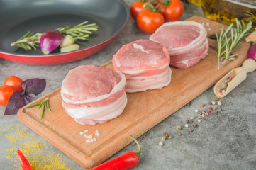 Three raw filet Mignon on a wooden board with spices, next to the pan, before cooking, side view