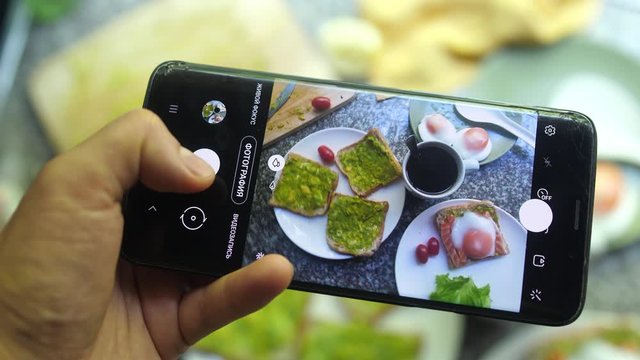 Taking Photos Of Healthy Avocado salmon Bruschetta with poached egg on broken Mobile phone