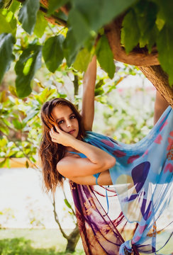 teen girl hanging on a tree like a monkey. Brunette with long hair hanging on a branch. Young attractive girl in a swimsuit in warm summer day. Travel, adventure, photo shoots in hot countries.