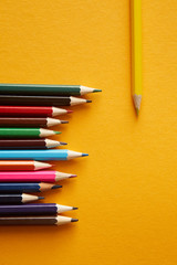 A set of colored pencils on a bright yellow background. One yellow pencil is placed separately.