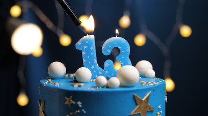 Birthday cake number 13 stars sky and moon concept, blue candle is fire by lighter. Copy space on right side of screen. Close-up
