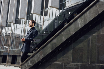 Photo of smiling businessman in coat and turtleneck with bagpack, talking on the phone