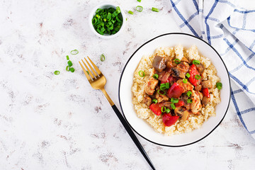 Bulgur and sauteed chicken, mushrooms, eggplants, paprika and tomatoes in a white bowl. Top view, overhead