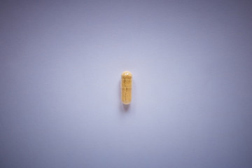 one yellow pill on a plain background