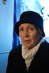 Portrait of an old woman. Grandmother in black clothes, a hat and a white scarf.