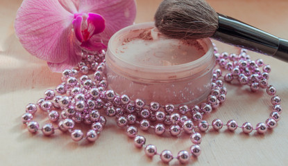 Mineral powder with a brush and an orchid with beads. Women's cosmetics. Natural cosmeics. Beauty and fashion.