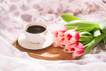 A cup of fragrant freshly ground coffee with a fresh bouquet of white-pink tulips on a wooden tray. Horizontal view