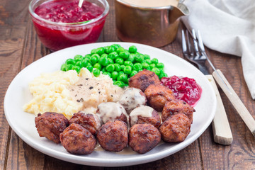 Traditional swedish meatballs served with mashed potato, green peas, cream sauce and cranberry jam, on plate, horizontal