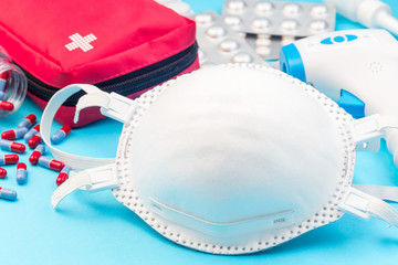 Different medicine on the table, mask, infrared body thermometer, first aid kit,  pills, on a blue...