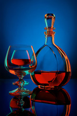 Cognac decanter and wine glasses in colored light on a blue background