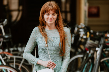 Stylish urban young redhair woman in a fashionable green dress posing in the street. European modern cute model girl enjoys a walk in the city. Spring fashion.